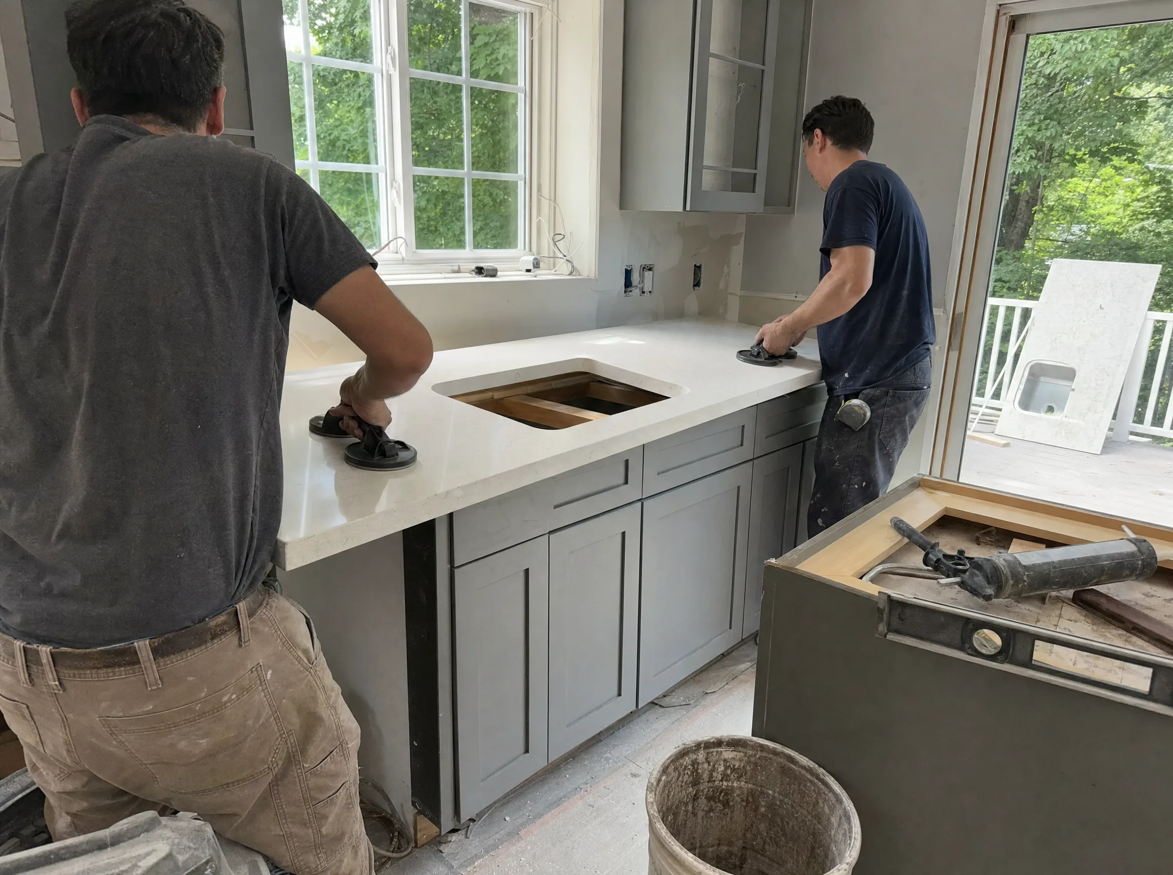Two installers setting a quartz countertop slab onto new kitchen base cabinets