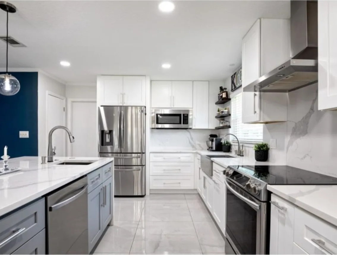 After: Kitchen after the remodel: dated oak cabinets replaced with white and gray cabinets, quartz counters and a marble look backsplash