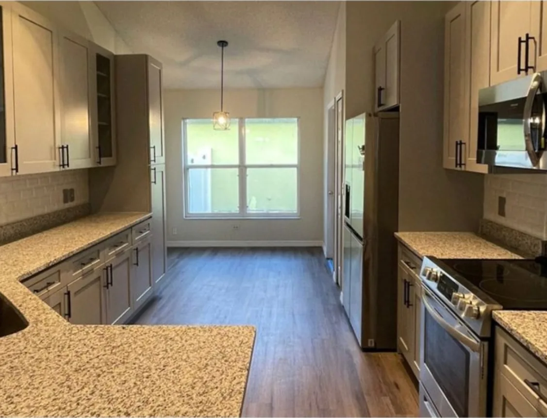 After: Kitchen after the remodel: cherry kitchen replaced with gray cabinets, granite and wood look flooring