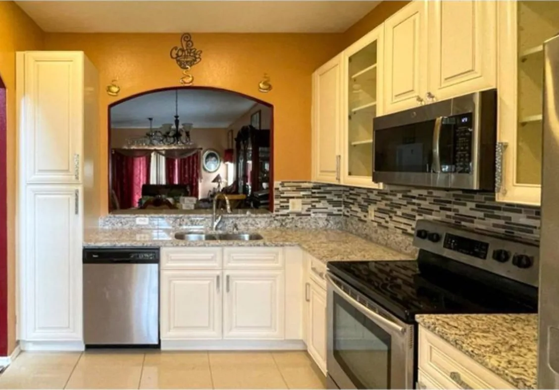 After: Kitchen after the remodel: oak cabinets replaced with white cabinets, granite and a stone backsplash