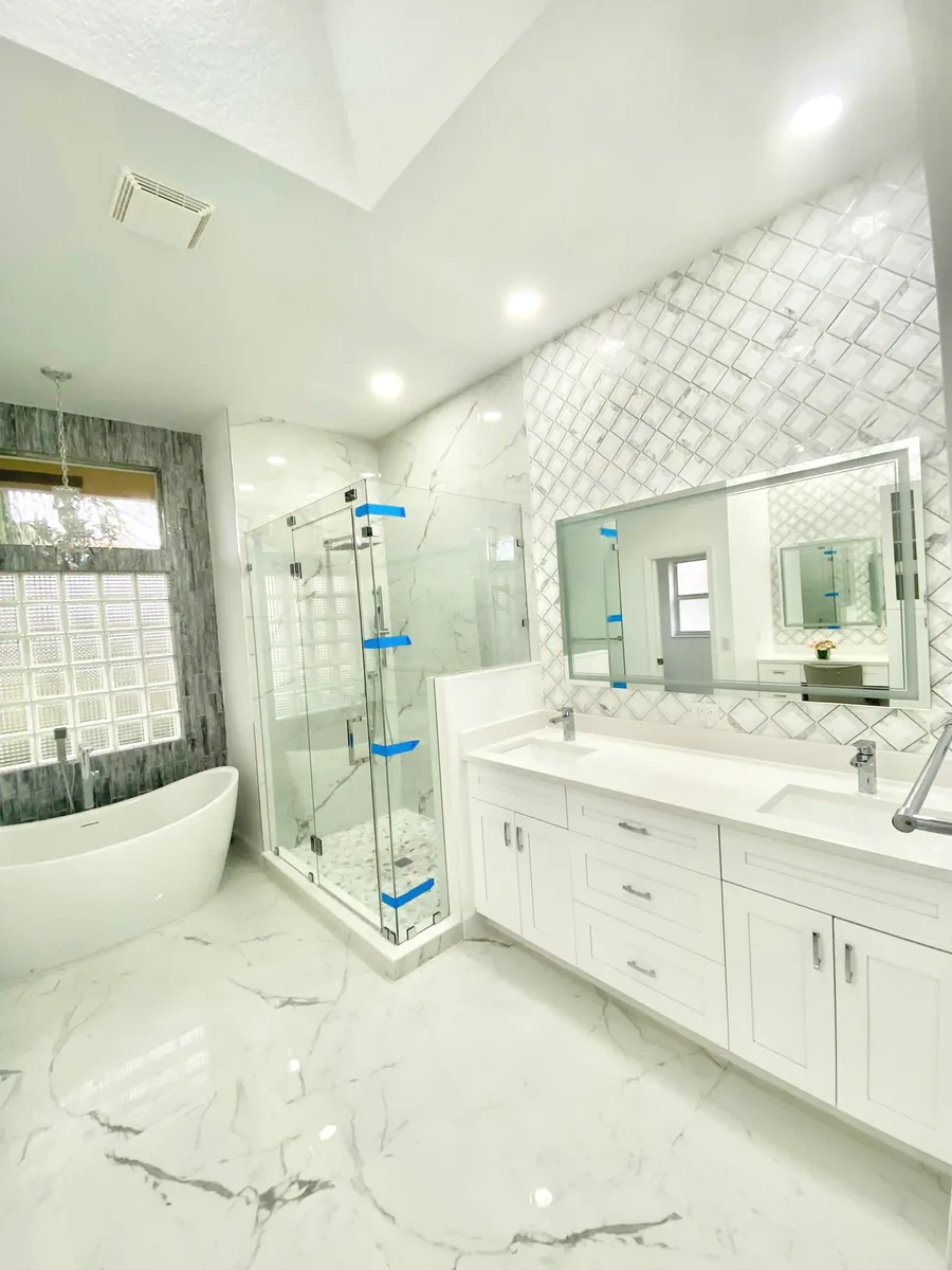 White marble look bathroom with frameless shower, freestanding tub and double vanity