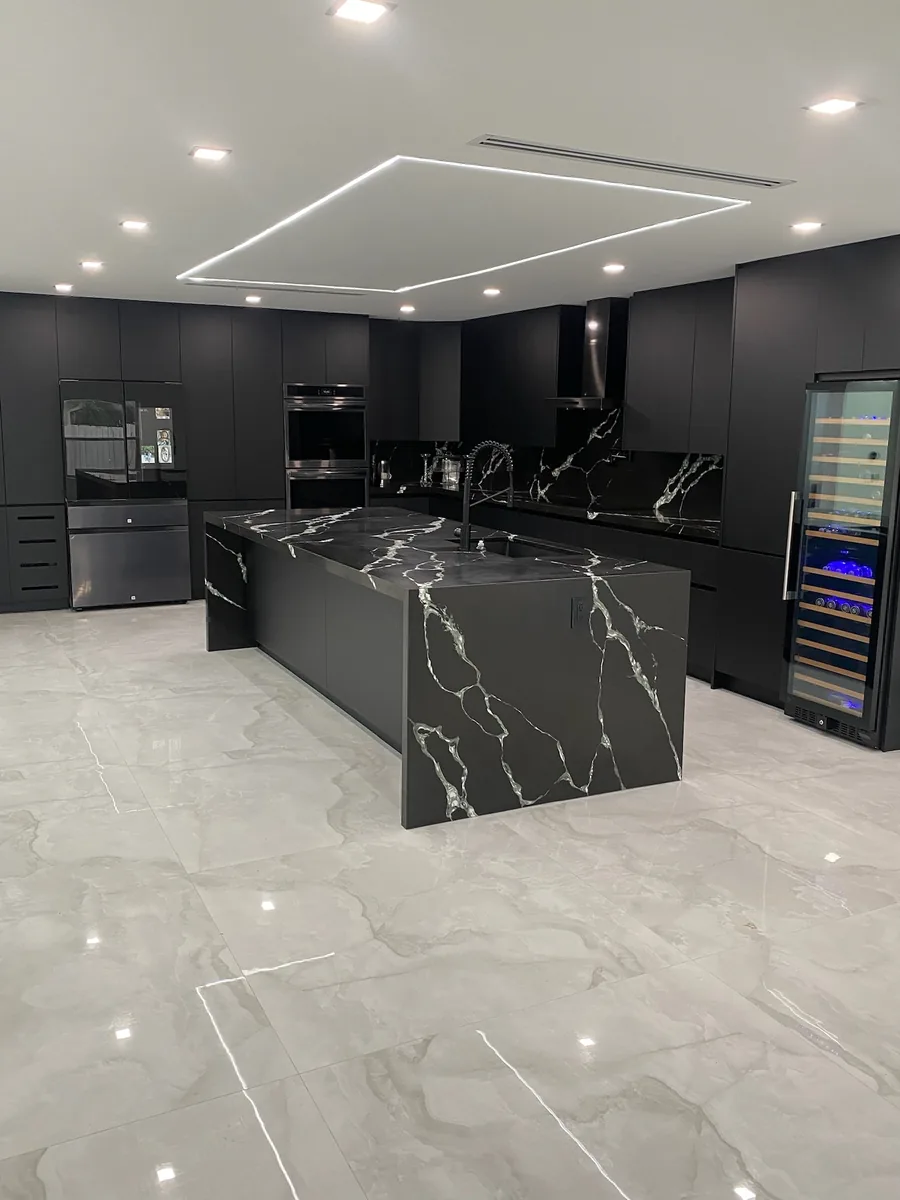 Black veined quartz waterfall island in a charcoal kitchen with built in wine fridge and large format porcelain floor