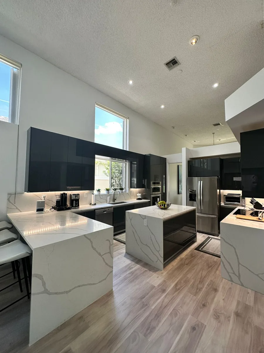 Vaulted kitchen with dark gloss cabinets and two white quartz waterfall islands with gray veining
