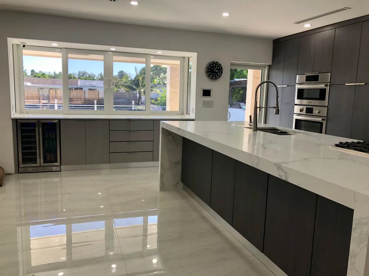 Remodeled kitchen with dark lower cabinets, white quartz waterfall island and polished porcelain floor