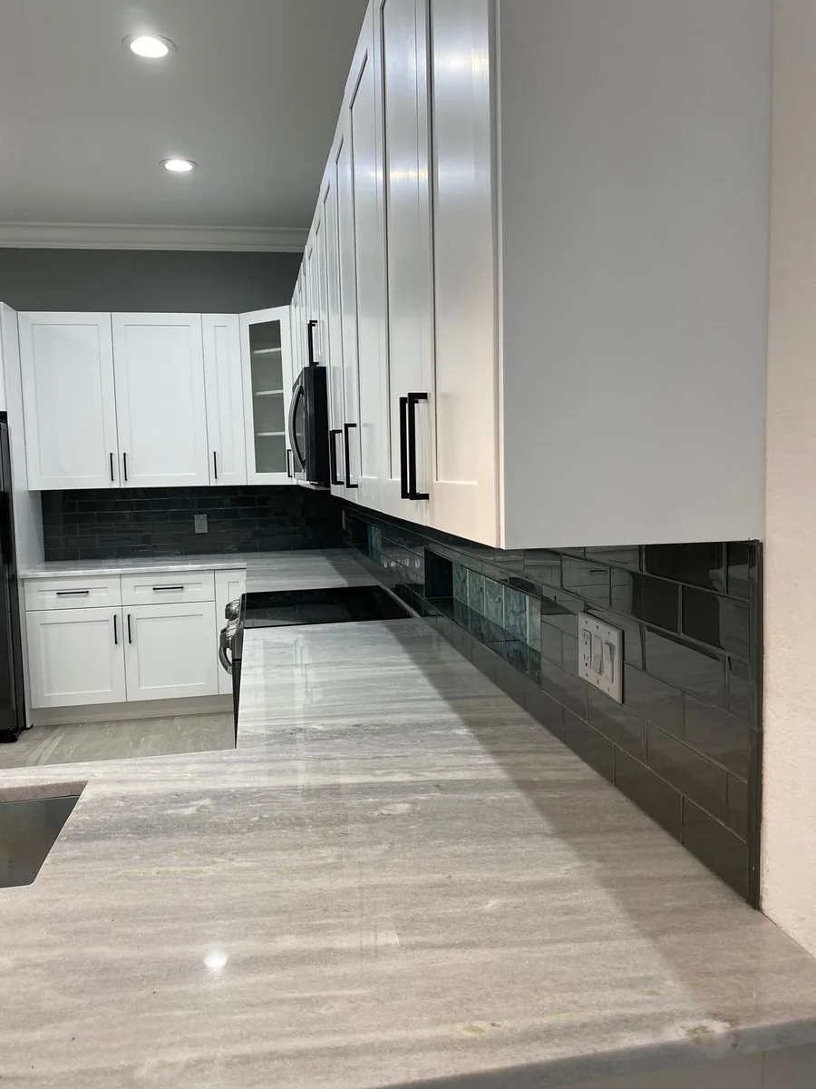 White shaker upper cabinets over a black glass tile backsplash and gray quartzite countertop