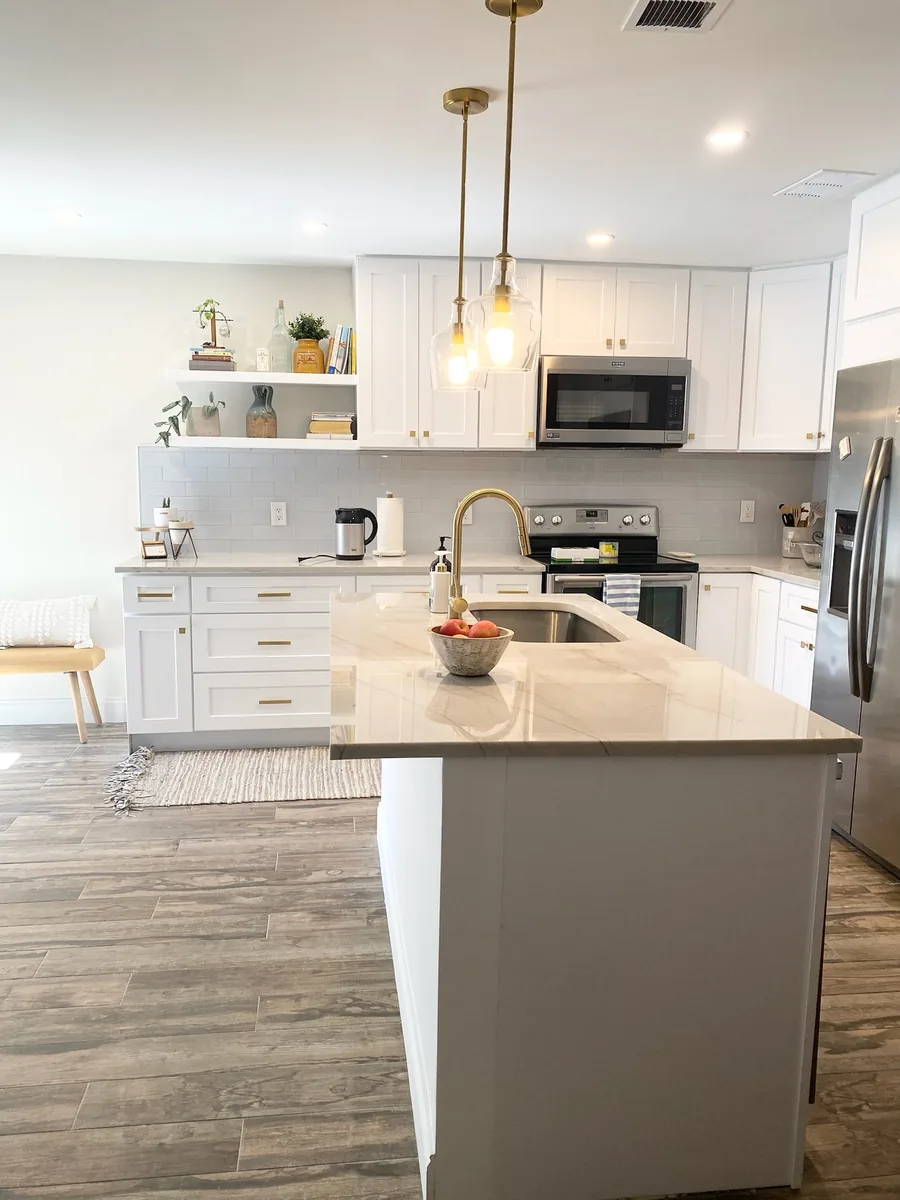 White shaker island with a quartz top, brass faucet and pendant lights over the sink