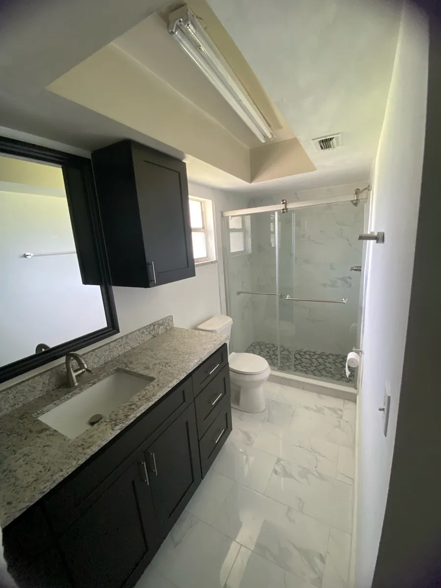 Dark vanity with a granite top beside a new glass shower