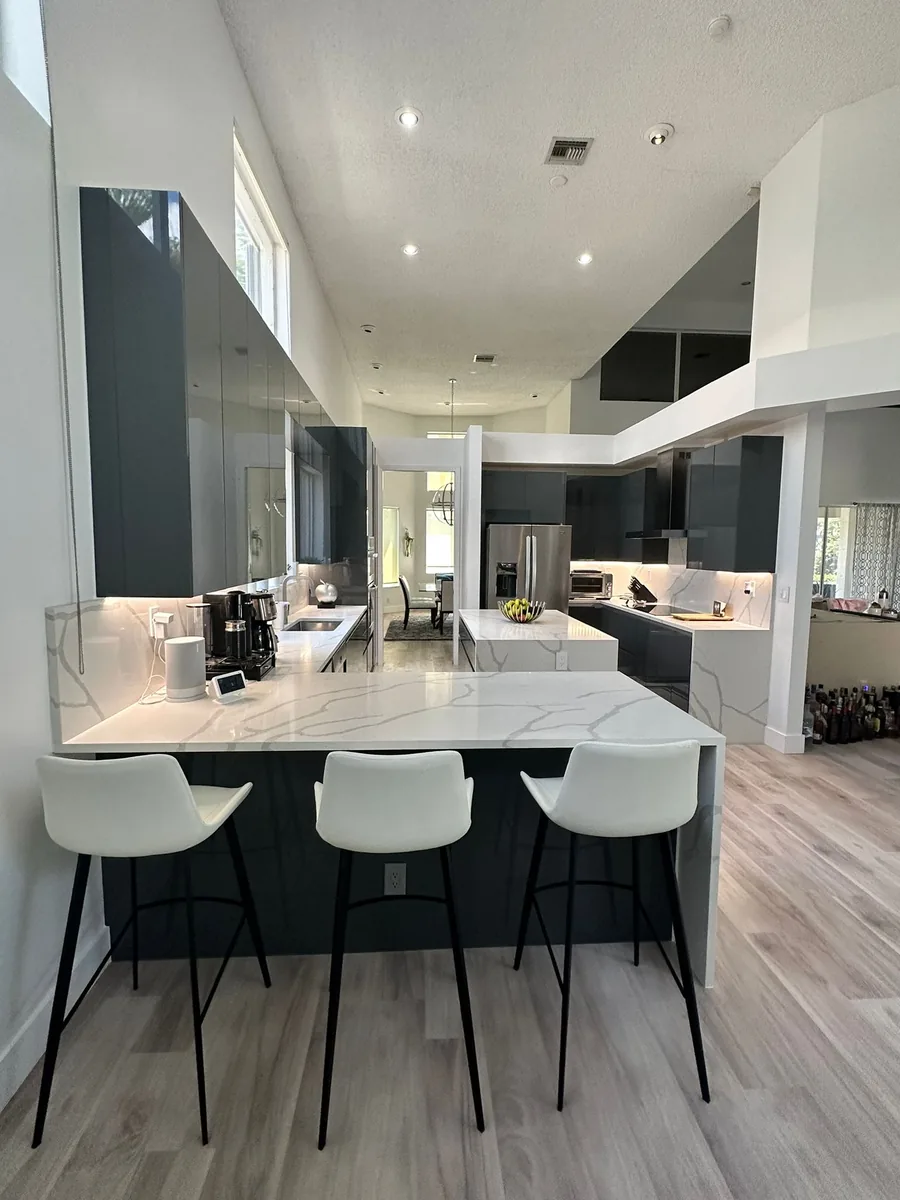 Open plan kitchen with a white veined quartz island, three stools and a vaulted ceiling